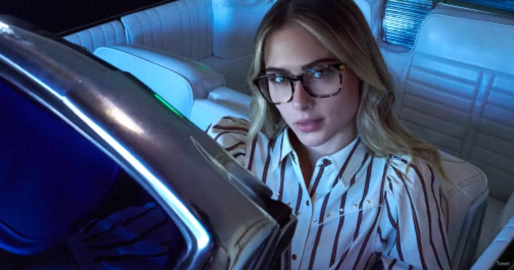 A girl staring into the camera wearing anti glare glasses in the car at night