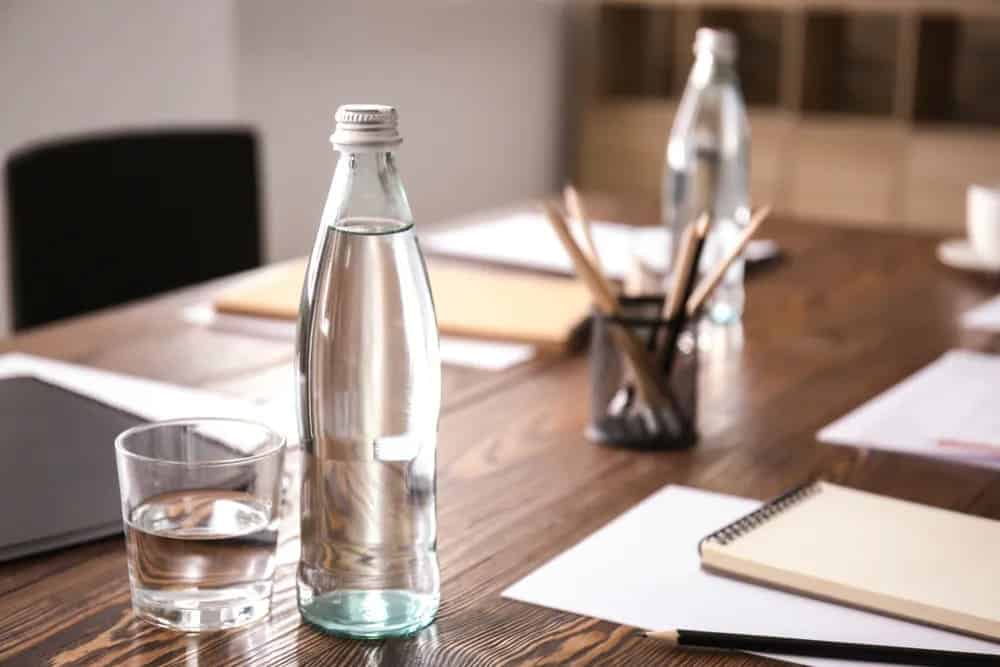 A glass water bottle sitting on a desk alongside a glass