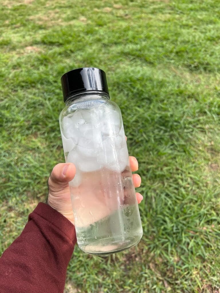 A hand holding Pureif You glass water bottle with iced water