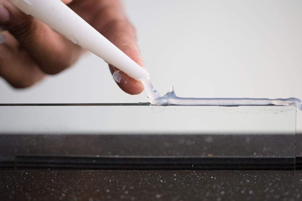 A hand putting glue on a glass window pane