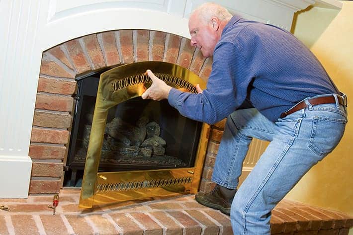 A man taking out the glass fram out of the gas fireplace