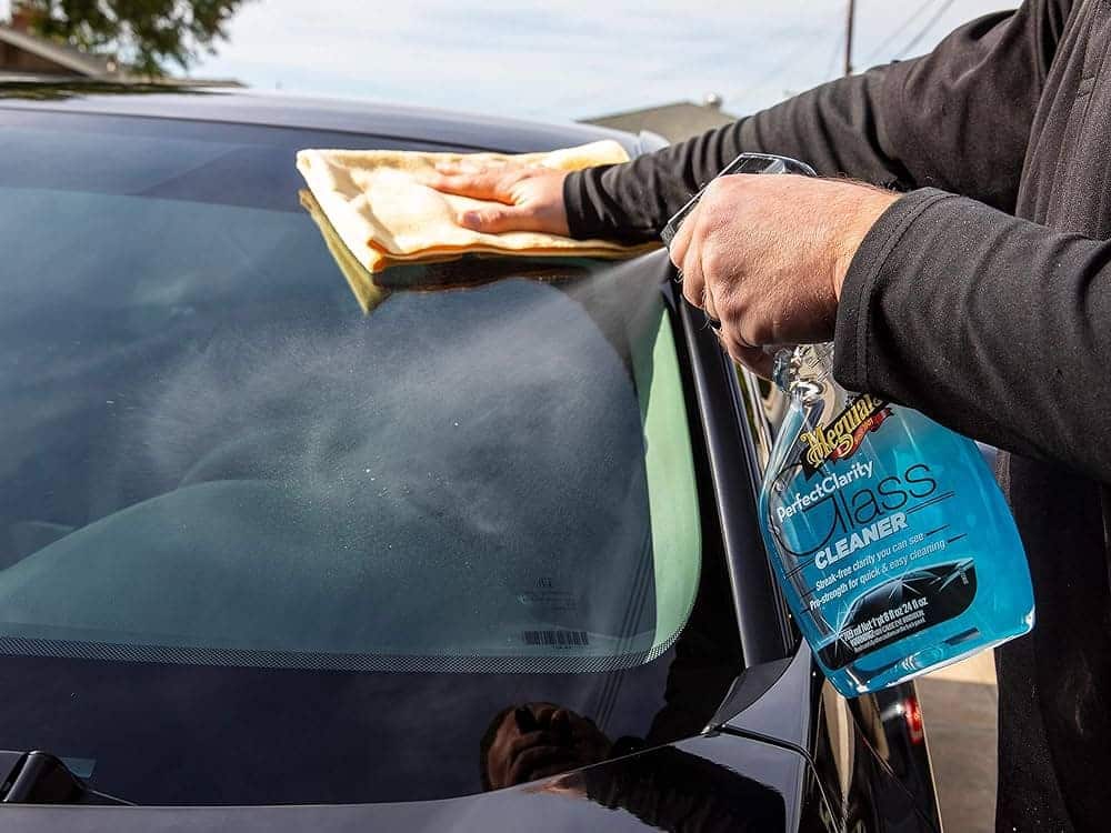 A person cleaning black car with Meguiar's clarity auto glass cleaner