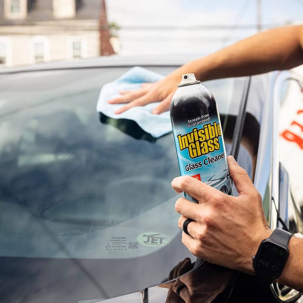 A person holding invisible glass cleaner and clenaing car with a cloth