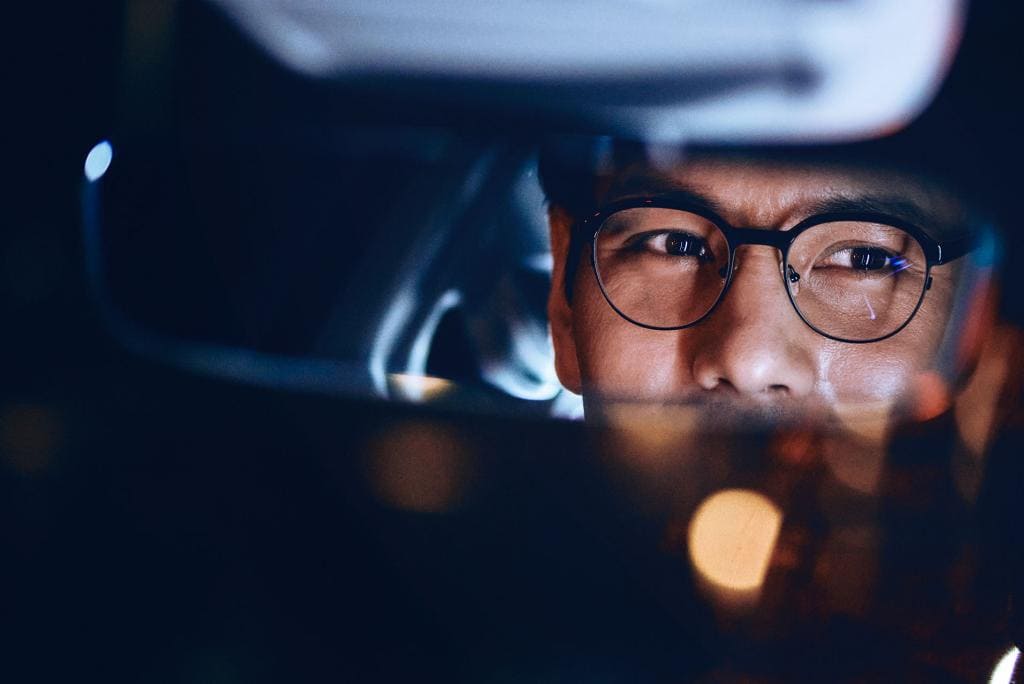 A person looking into the rearview mirror wearing night driving glasses in car