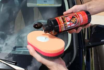 A person pouring Wolgang auto glass polish onto the scrub