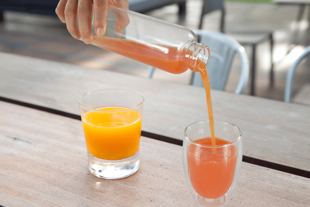 A person pouring orange juice in a glass from a water bottle