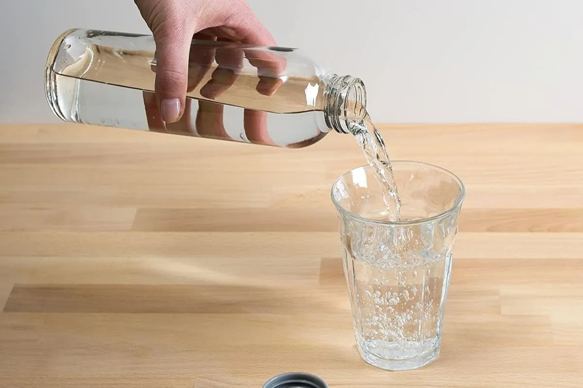 A person pouring water in a glass from a glass bottle