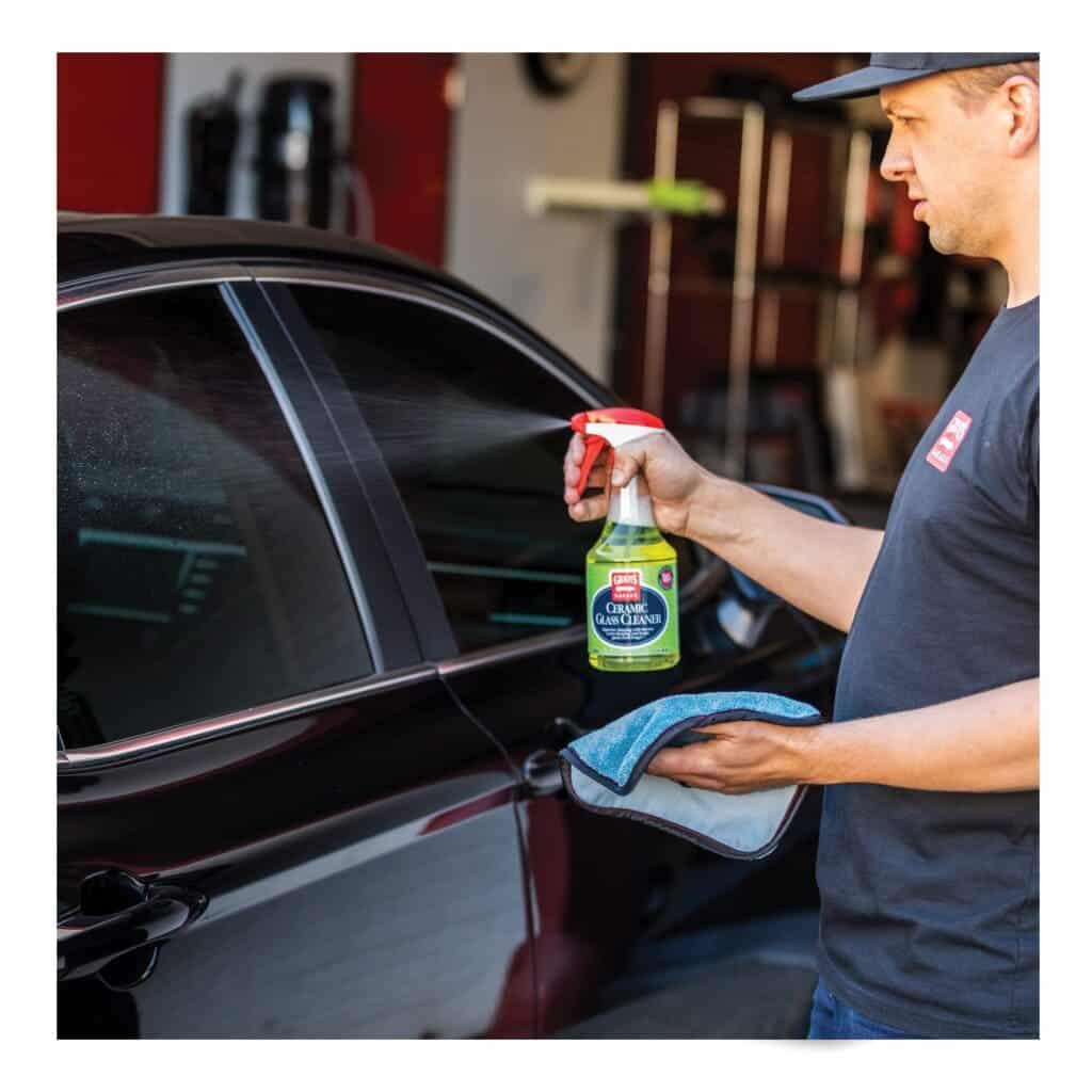 A person spraying Griot's ceramic cleaner on a black car