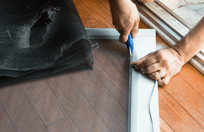 A person trimming the screen material off a sliding window