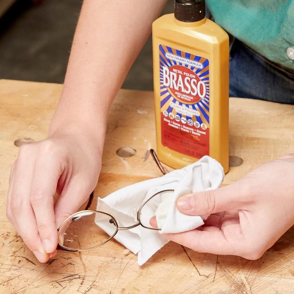 A person using Brasso metal polish on glasses with a white cloth