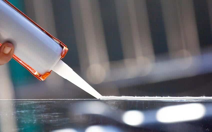 A person using a glue nozzle to bond a window sill