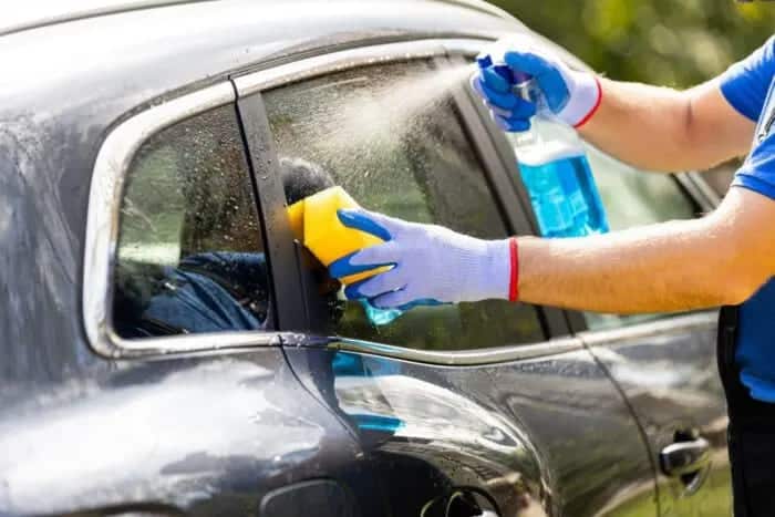 A person wearing gloves and spraying and scrubbing car