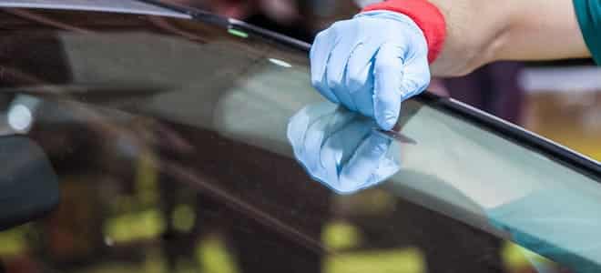 A person wearing gloves scraping off glue from a car windshield