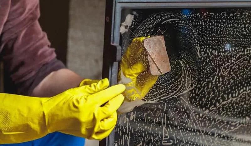 A person wearing gloves scrubbing off the fireplace glass