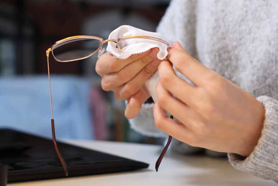 A person wiping off their glasses with a cloth