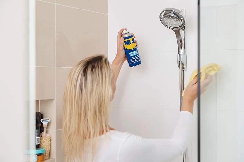 A woman removing hard water stains from a glass shower door