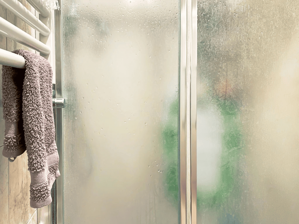 hard water stains on a bathroom shower door alongside a towel hanging