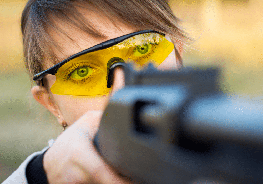 A young girl with a gun for trap shooting and shooting glasses aiming at a target