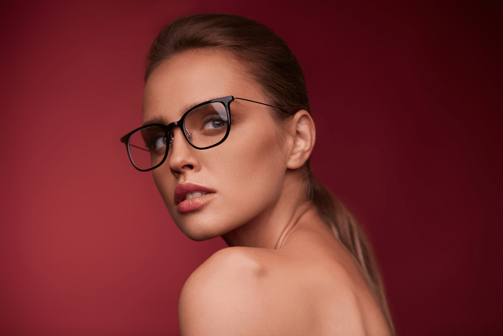 Attractive woman in square eyeglasses looking at camera on red background