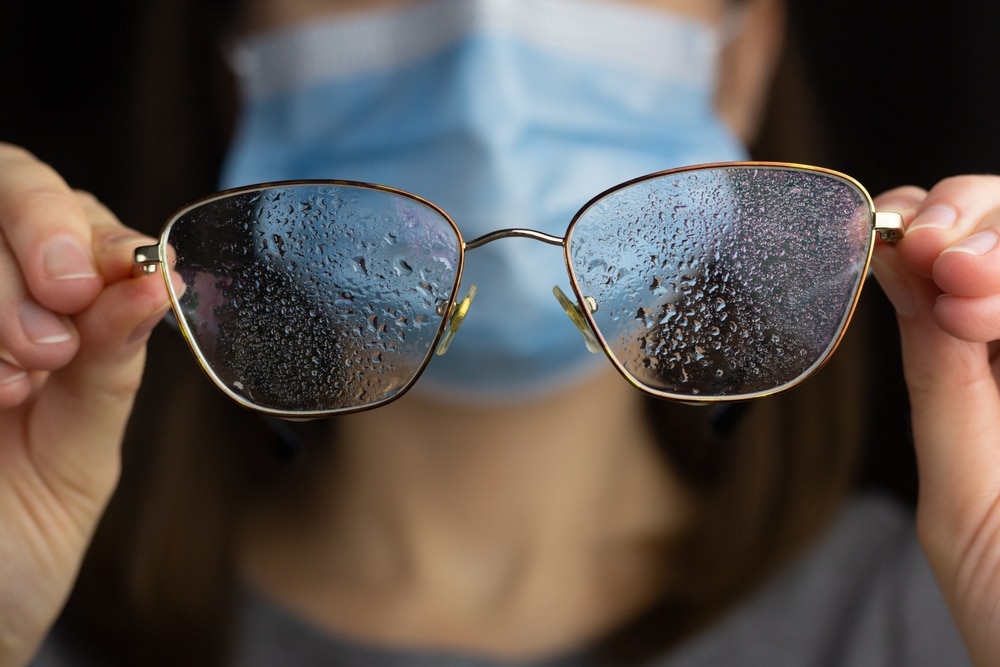 A Woman In Protective Face Mask holding her sprayed aanto fog glasses 