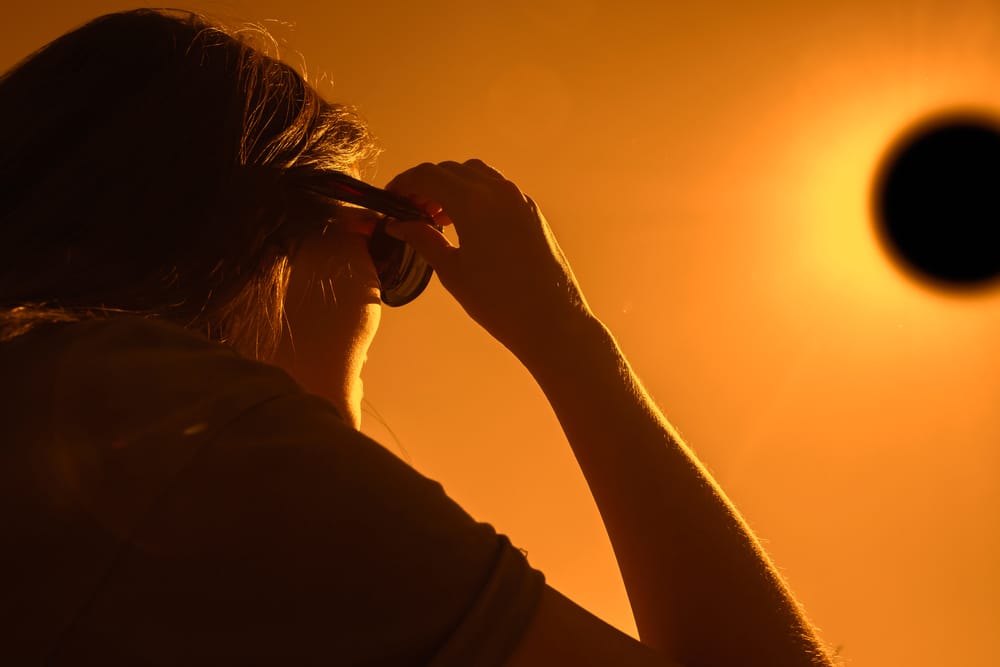 Woman is looking on solar eclipse through eclipse sunglasses