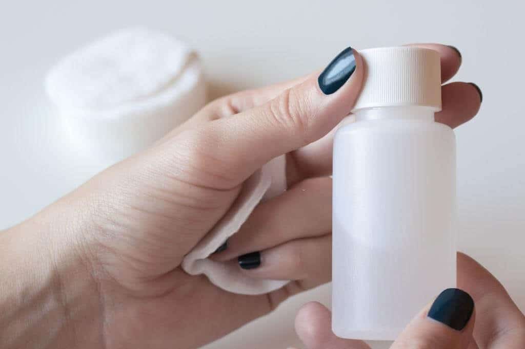 a hand of a lady holding a bottle of nail polish remover and cleaning pads