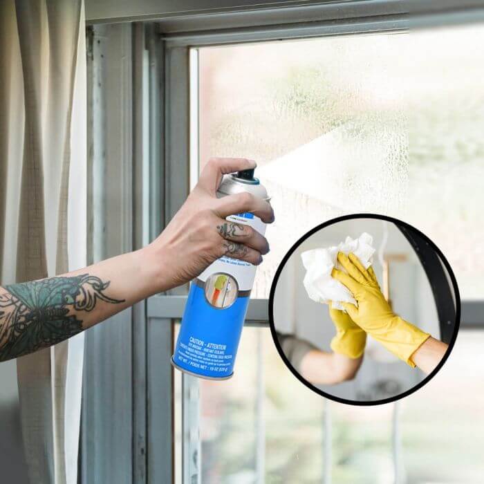 a man holding a glass cleaner spray bottle and spraying on thr glass window