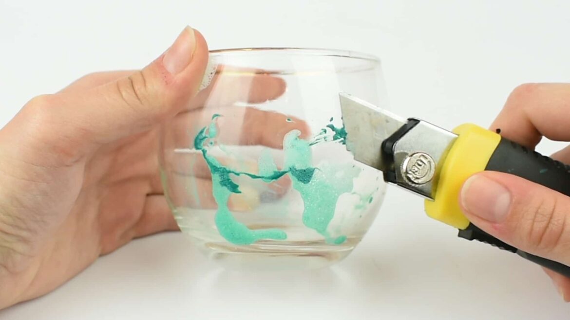 a person holding a glass in one hand and removing the paint using a cutter