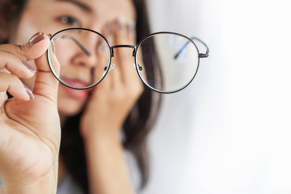 Asian woman hand holding eyeglasses having problem with eye pain blur vision