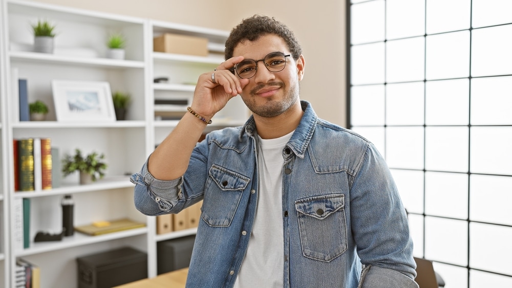 Smiling Bearded Man Adjusting Glasses In A Modern Office Setting