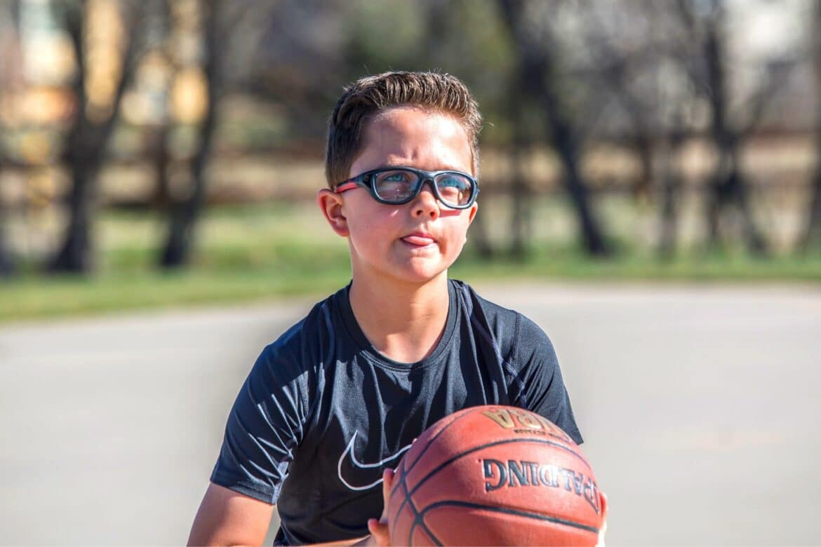 A view of a boy holding a basket ball wearing glasses