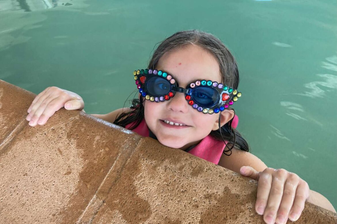 A view of a little girl wearing swimming glasses while in the pool