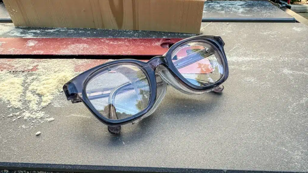 A pair of eyeglasses resting on a work surface with wood dust scattered around A pair of eyeglasses resting on a work surface with wood dust scattered around