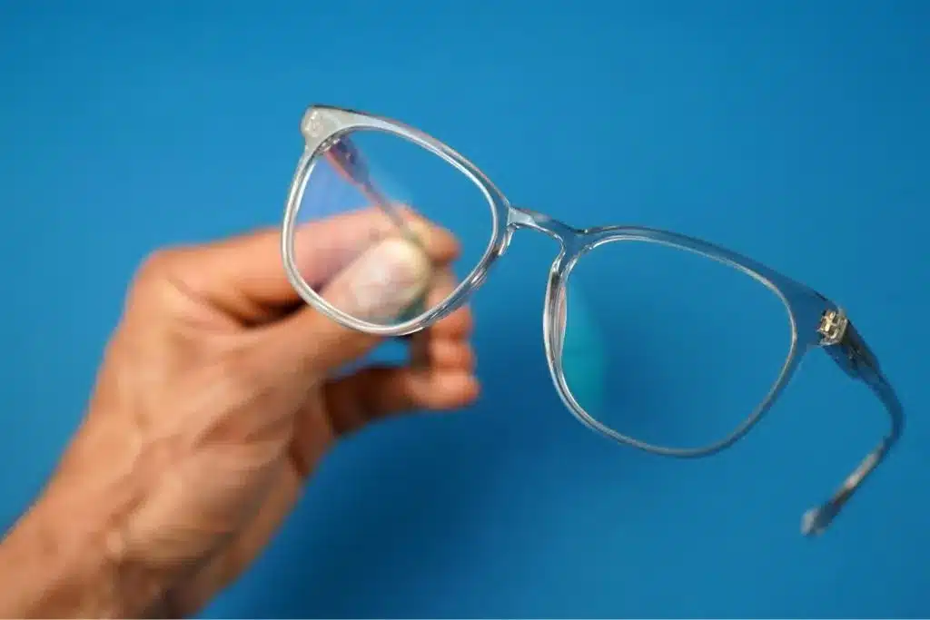 A person holding a pair of clear eyeglasses against a blue background A person holding a pair of clear eyeglasses against a blue background