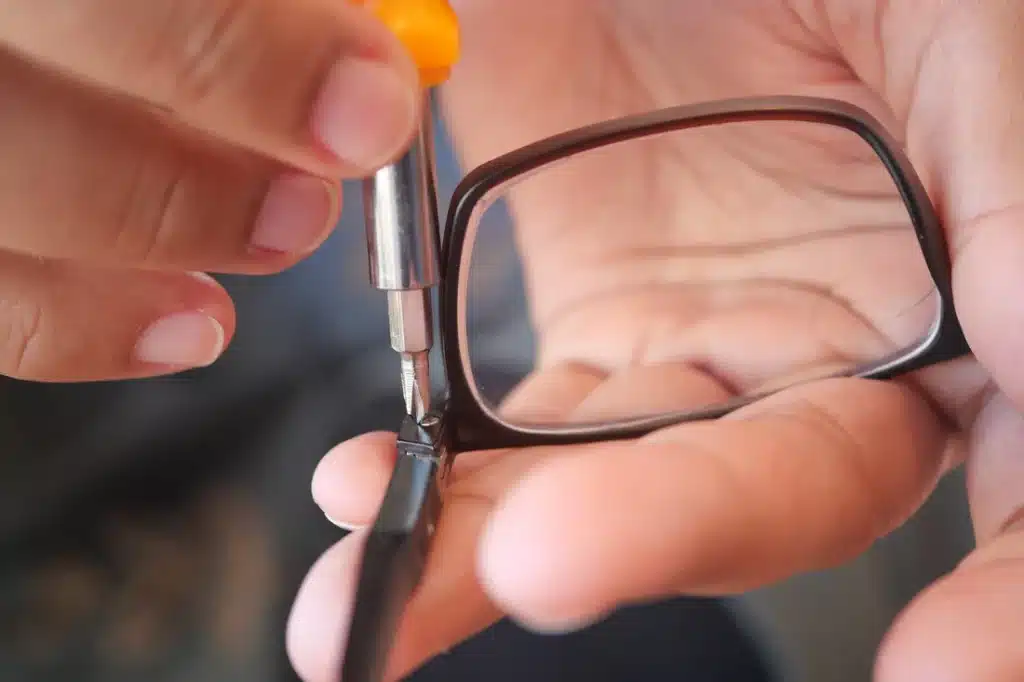 A person using a screwdriver to tighten a screw on the frame of eyeglasses A person using a screwdriver to tighten a screw on the frame of eyeglasses