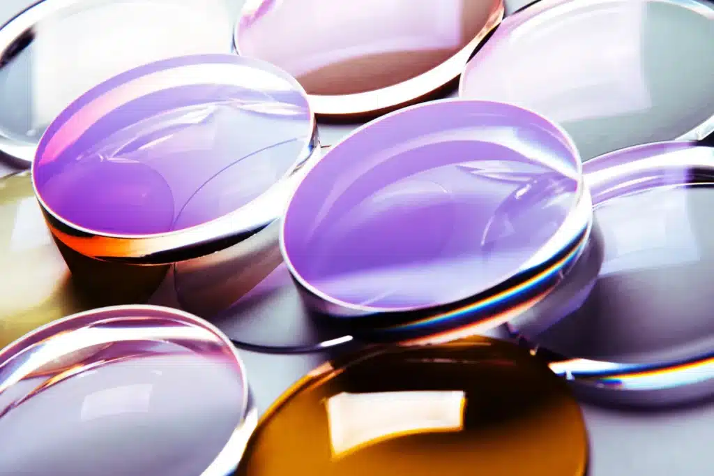 A close up of various eyeglass lenses in different colors showcasing lenses with a purple tint reflecting light from their smooth surfaces A close up of various eyeglass lenses in different colors showcasing lenses with a purple tint reflecting light from their smooth surfaces