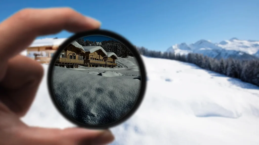 A hand holding a polarized lens showing a clear view of a snow covered landscape with cabins in the distance A hand holding a polarized lens showing a clear view of a snow covered landscape with cabins in the distance